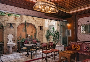A cozy room with a brick wall, a round table with chairs, a wooden sofa, and a chandelier.
