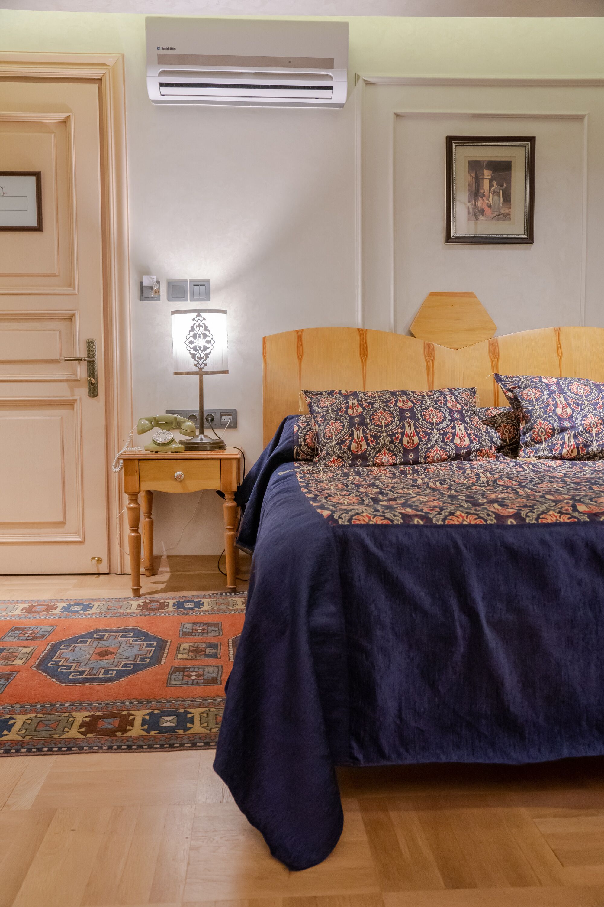 Ein Schlafzimmer mit einem Bett, einem Nachttisch mit Lampe, einer Wand-Klimaanlage und einem gemusterten Teppich.