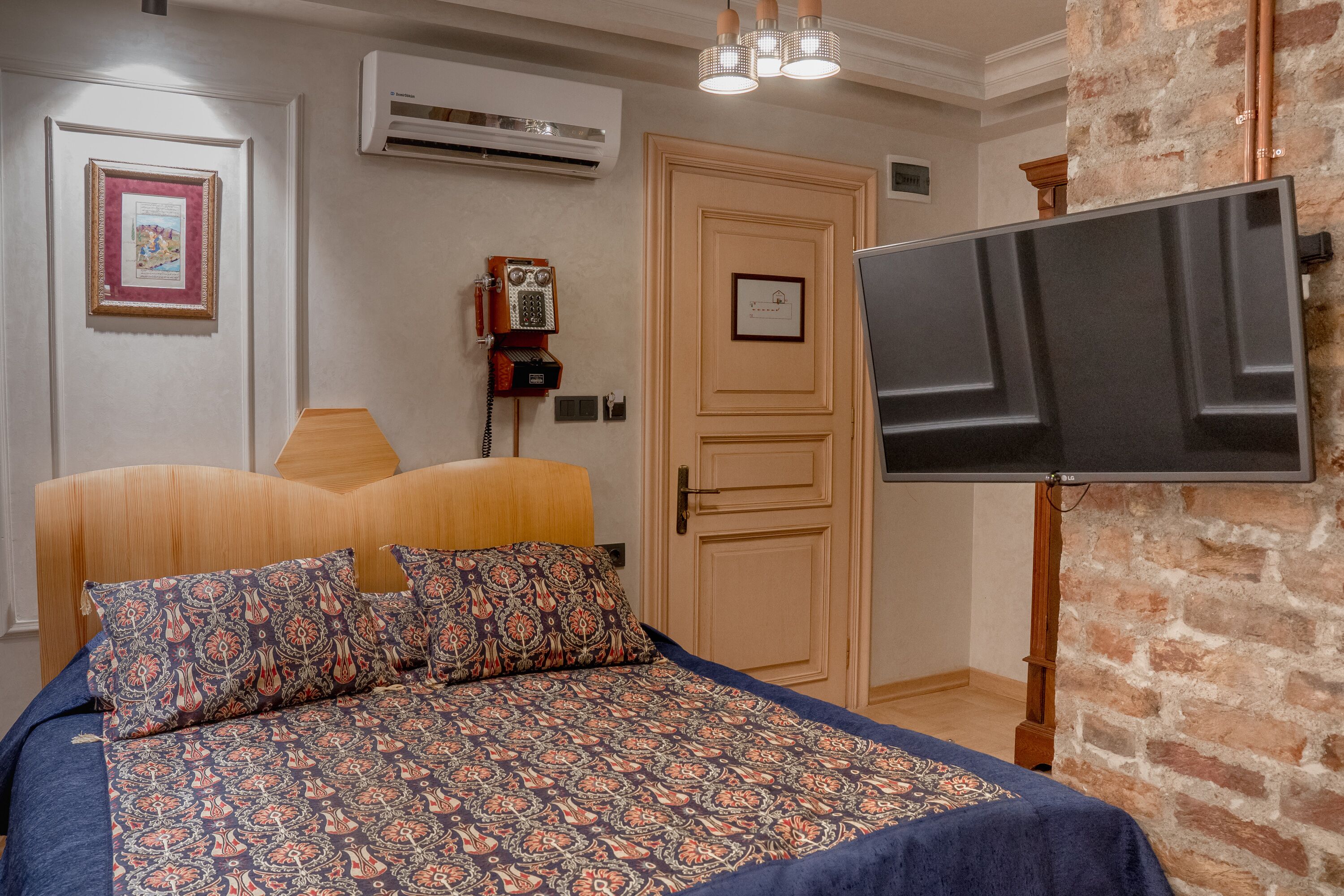 A bedroom with a bed, a television, a telephone, and a brick wall.