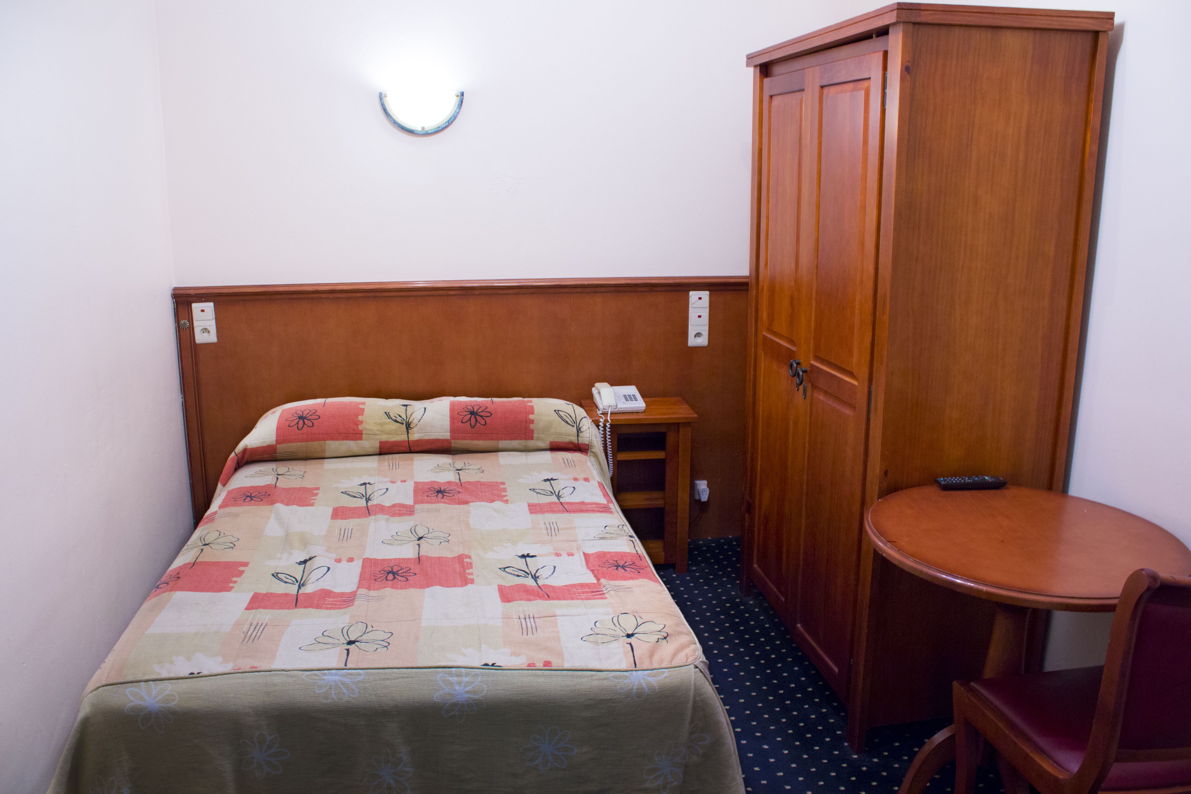 Habitación de hotel con cama, mesita de noche con teléfono, una pequeña mesa redonda y un armario.