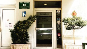 L’entrée d’un hôtel, avec un auvent vert sur lequel est inscrit le mot « HÔTEL » et une enseigne indiquant « Hôtel Continental, 18, place de la Constitution, 1060 Bruxelles ».