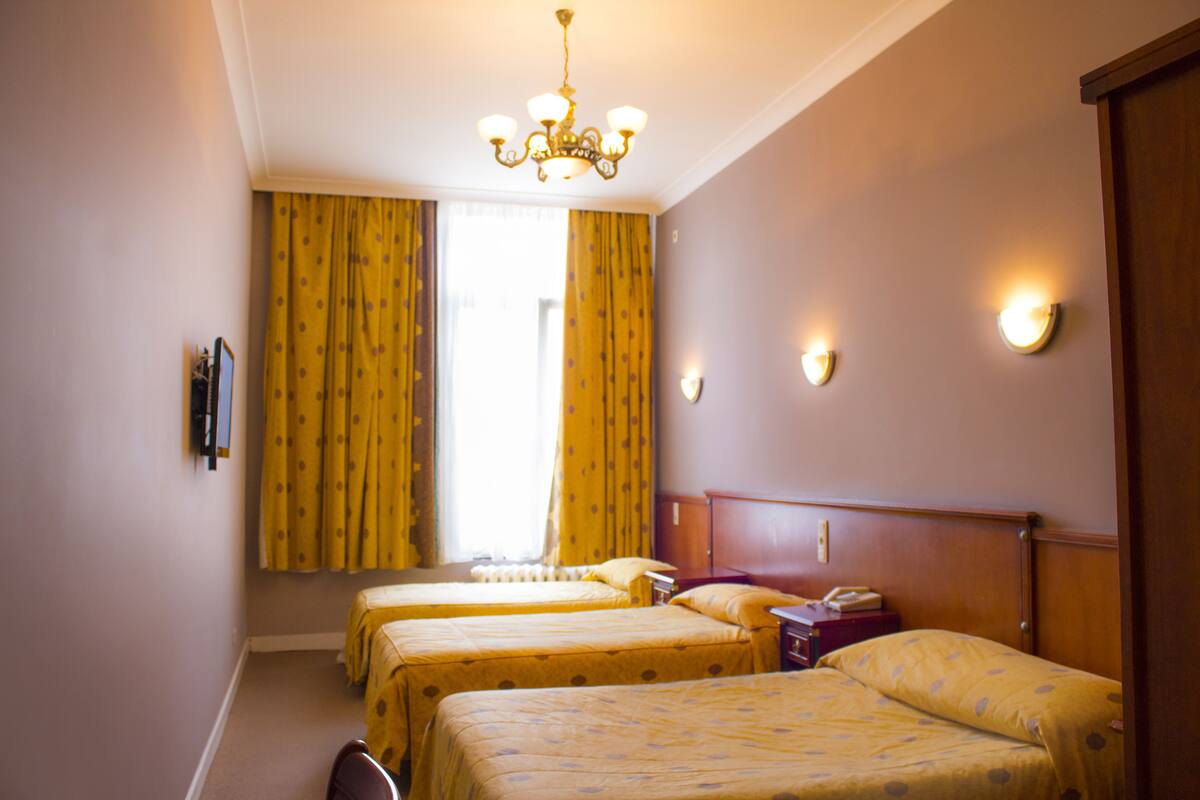 Ein Hotelzimmer mit zwei Betten, einer Kandelaber, einem Fenster mit Vorhängen und Wandleuchten.