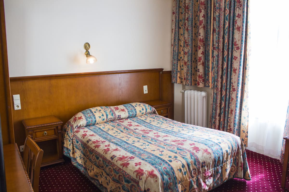 Ein Schlafzimmer mit einem hölzernen Kopfende, einer blumigen Tagesdecke, einem Nachttisch und einem Sessel.