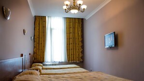 Une chambre d’hôtel avec deux lits, un lustre, une télévision et une fenêtre avec des rideaux.