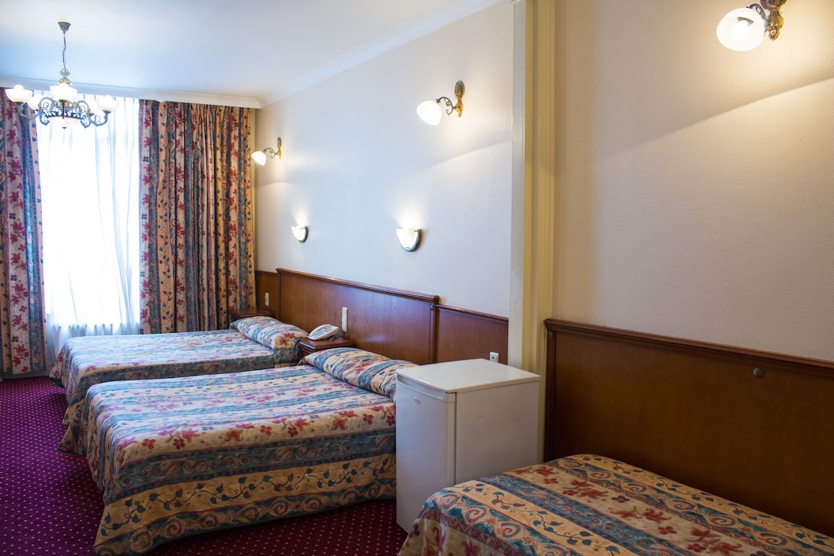 Ein Hotelzimmer mit zwei Betten, einem kleinen Kühlschrank, einem Holzkopfende und einer Kandelaberleuchte.