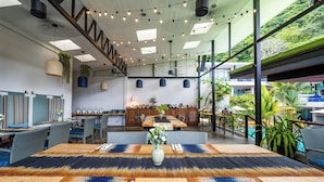 A modern dining area with a long table, hanging plants, and a view of a lush green hillside.