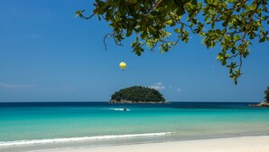 A beach with clear turquoise water, a sandy shore, and a small island in the distance.