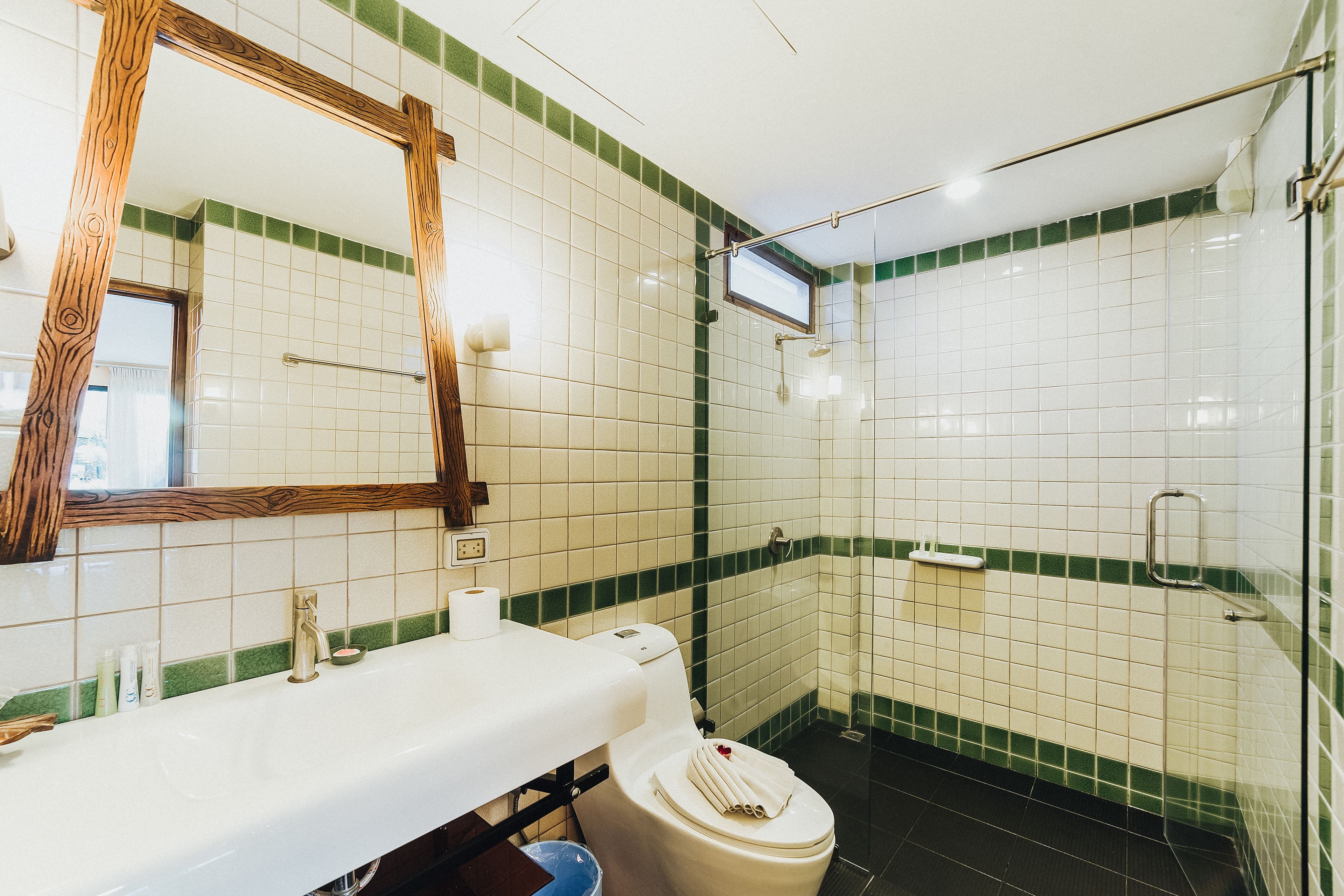 A bathroom with a white sink, mirror, and toilet, green-tiled walls, and a shower area.