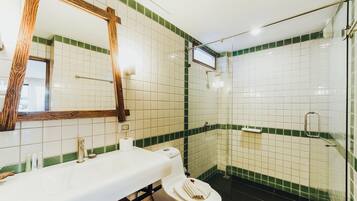 Un baño con lavamanos, espejo e inodoro blancos, paredes con azulejos verdes y zona de ducha.