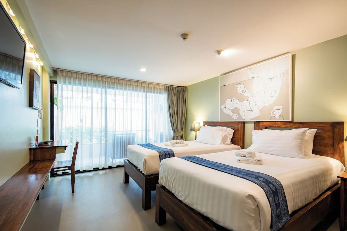 A hotel room with two beds, a desk, a chair, a TV, and a large window with curtains.