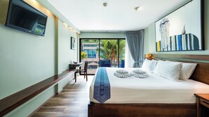 A hotel room with a large bed, a flat-screen TV mounted on the wall, a desk with a chair, and a view of the outside through a large window.