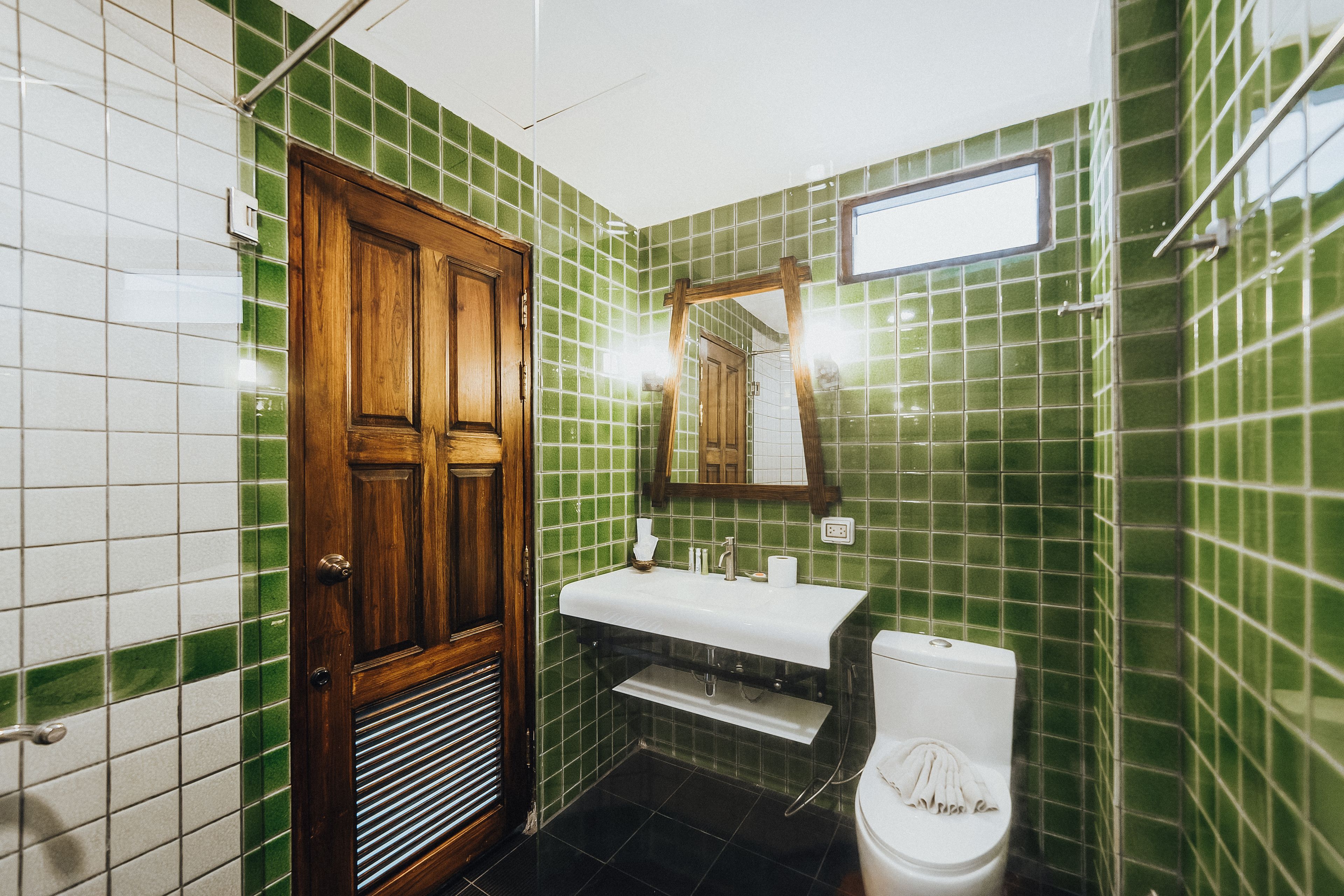 A bathroom with green tiled walls, a wooden door, a white sink, and a toilet.
