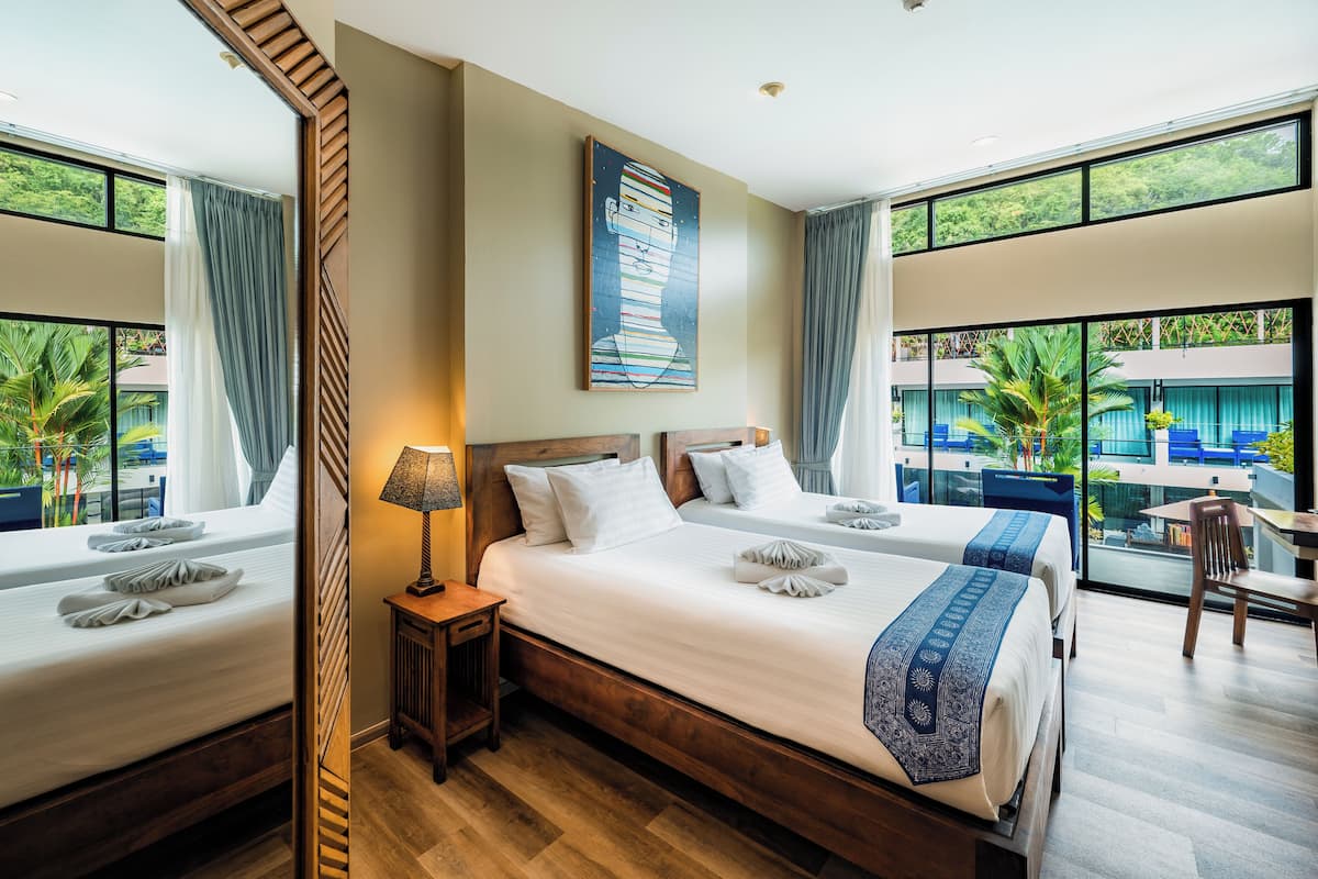A hotel room with two beds, a large window, a painting on the wall, and a view of the outside.
