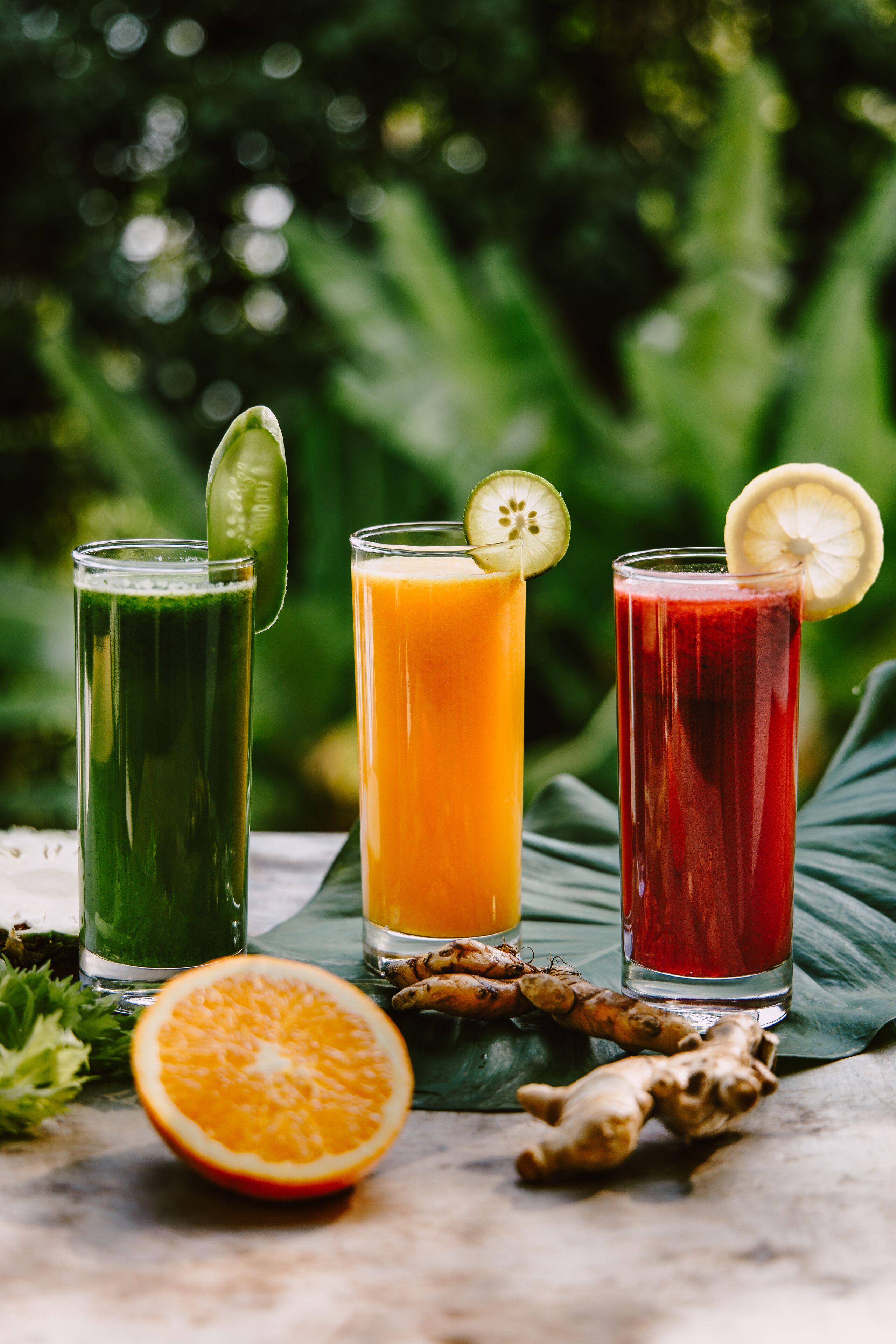 Three tall glasses of juice with lime slices, placed on a table with a green leaf and ginger root beside them.