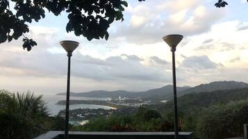 A bench with two street lamps, overlooking a coastal landscape with hills and a body of water.