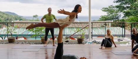 A group of people practicing yoga on a wooden deck with a view of the ocean and hills in the background.