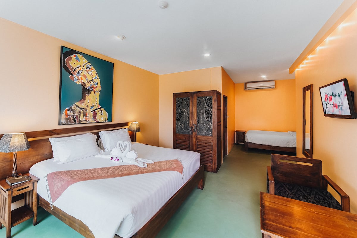 A hotel room with a large bed, a smaller bed, a wardrobe, a desk, and a chair.