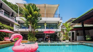 A swimming pool with a pink flamingo float, surrounded by modern buildings with balconies and outdoor seating areas.