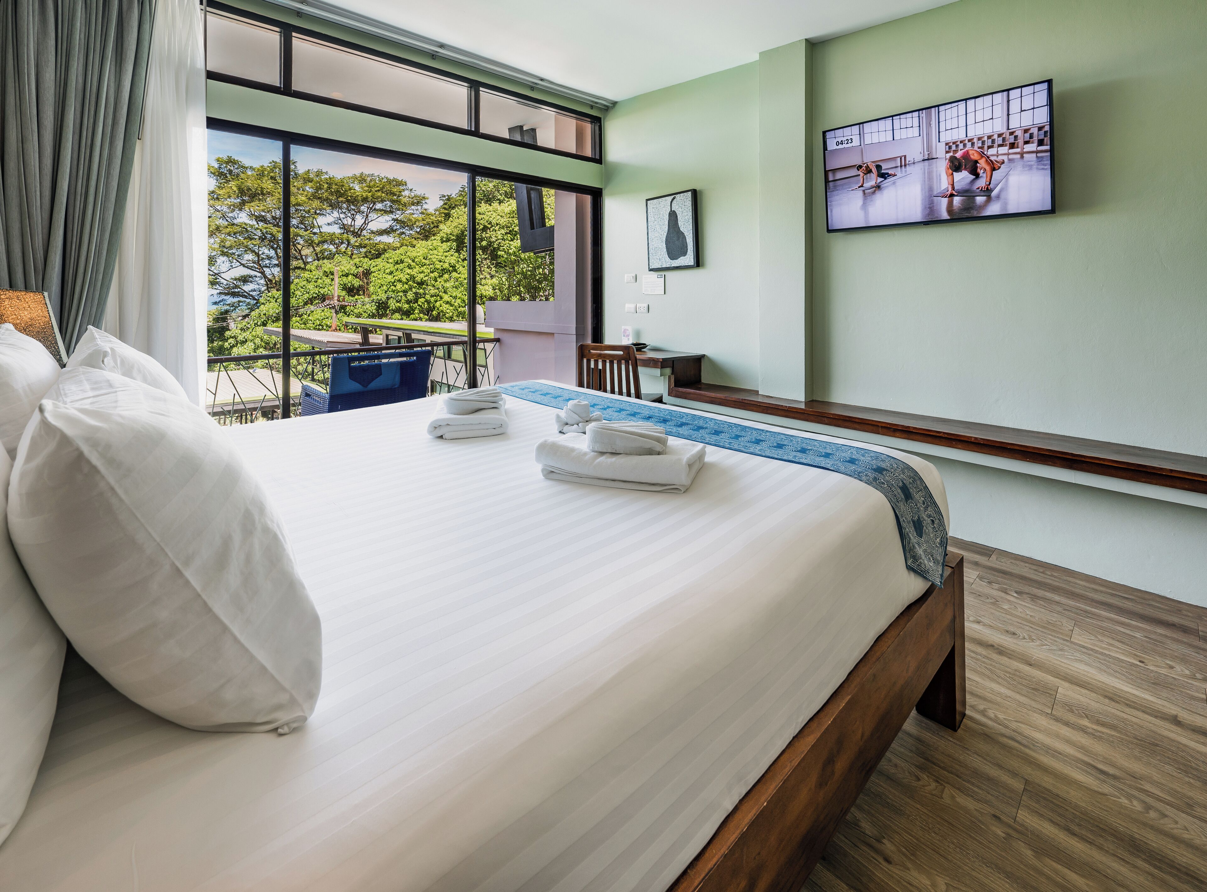 A hotel room with a large bed, a TV on the wall, and a view of the outdoors.