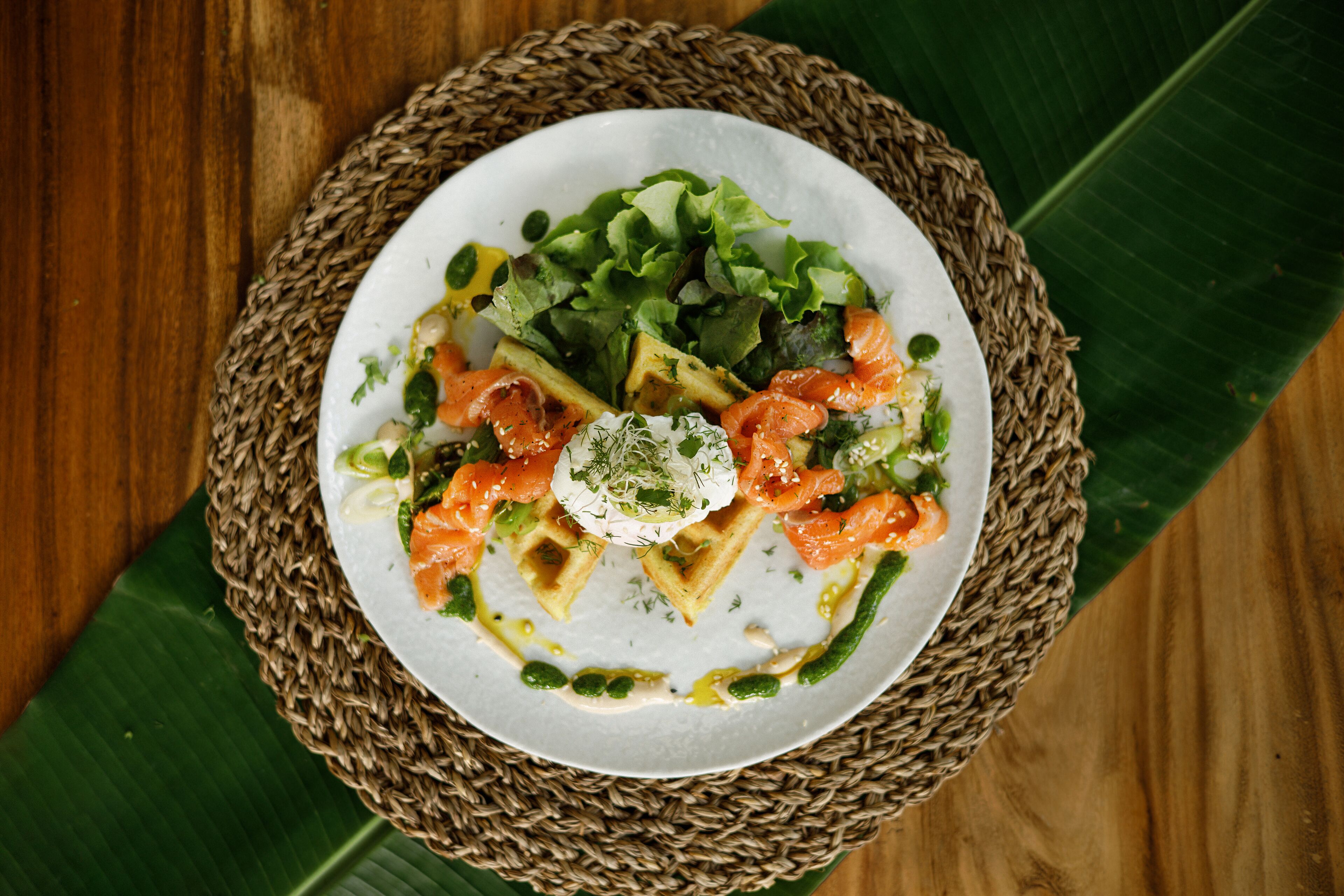 A plate of food with salmon, greens, and a dollop of cream on a woven mat.