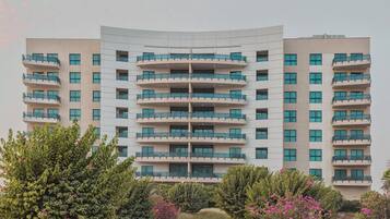Un hotel de diverses plantes amb una façana corba, balcons a cada planta i un jardí paisatjistic amb arbustos i flors.