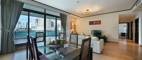 A modern living room with a glass dining table, wooden chairs, a white sofa, and a TV.