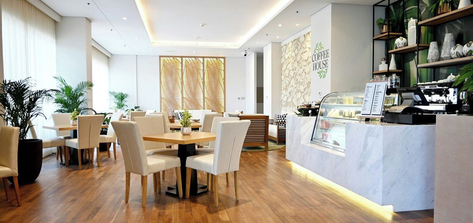 A modern coffee house interior with a wooden dining area, a counter with a coffee machine, and decorative plants.