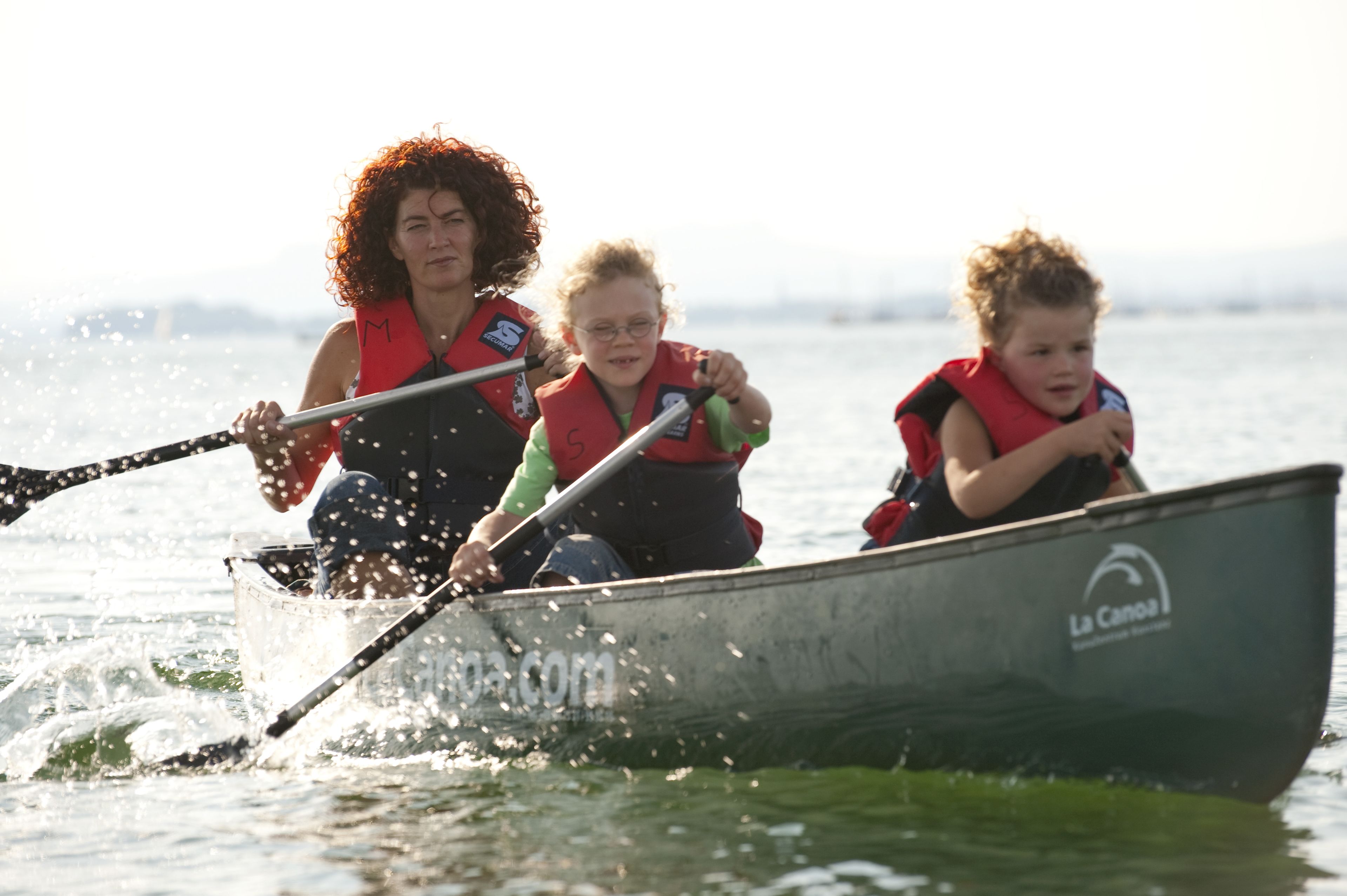Three people in a boat with a logo on the side.