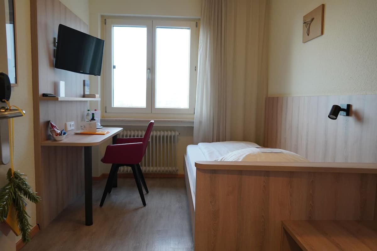 Une chambre d’hôtel avec un lit, un bureau, une chaise, une télévision et une fenêtre.