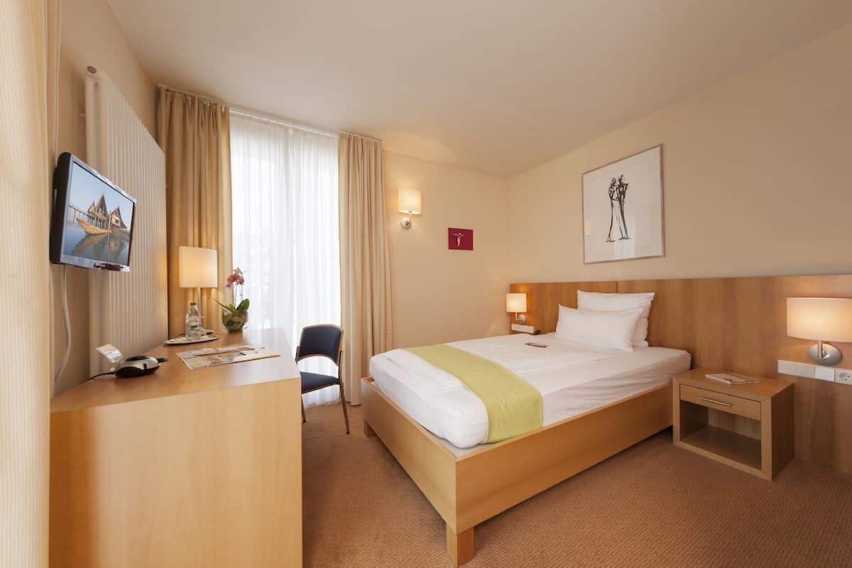 Une chambre d’hôtel comprenant un lit, des tables de chevet, un bureau avec un ordinateur, une chaise et un téléviseur.