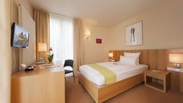 A hotel room with a bed, bedside tables, a desk with a computer, a chair, and a TV.