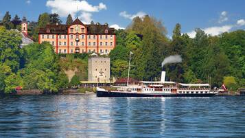 A historic building with a clock tower, a river with a boat, and lush greenery.