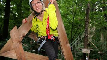 A person climbing a wooden structure in a forested area with ropes and harnesses.