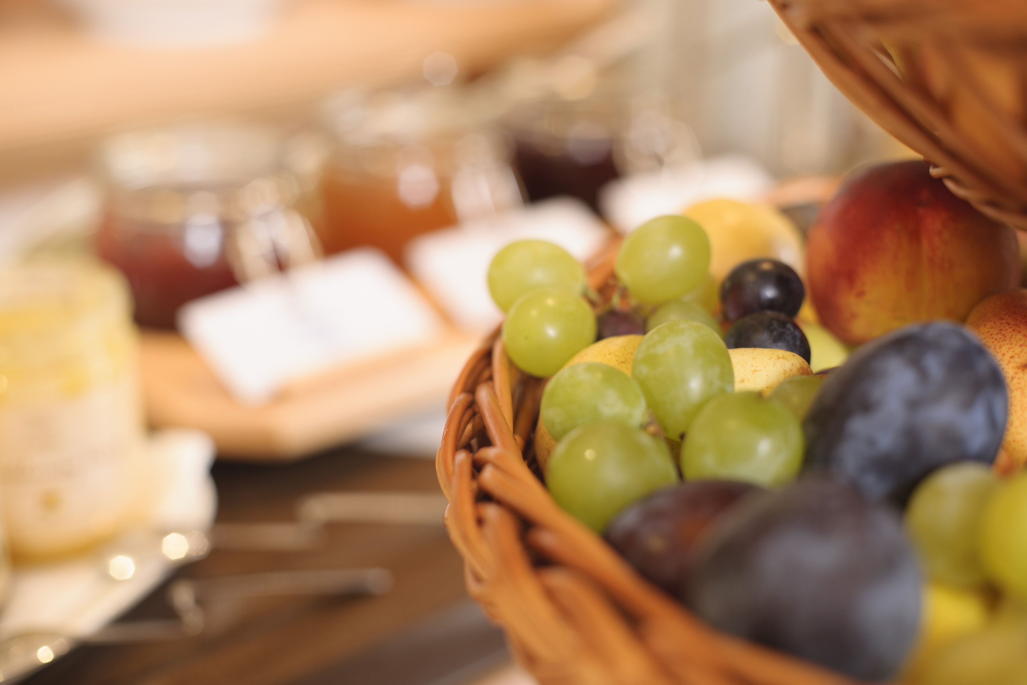 Una cesta de mimbre llena de frutas variadas, como uvas, ciruelas y un melocotón, sobre una mesa de madera.