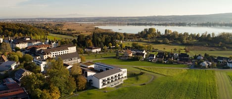 An aerial view of a hotel with multiple buildings, surrounded by green fields and a lake.