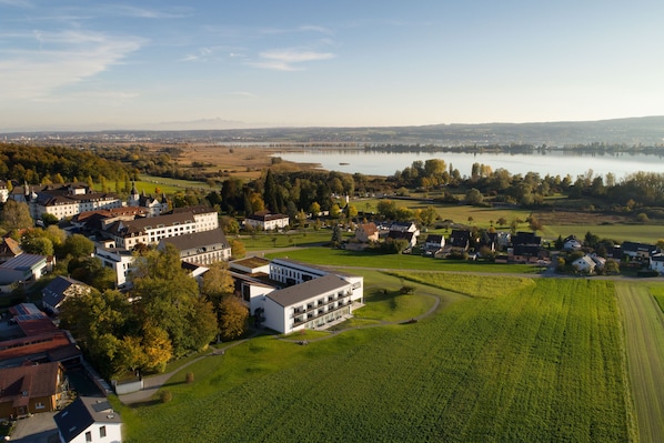 An aerial view of a hotel with multiple buildings, surrounded by green fields and a lake. - Hotel St. Elisabeth (Allensbach)