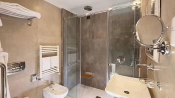 A modern bathroom with a glass-enclosed shower, a bidet, a sink with a glass soap dish, and a towel rack.