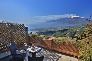 Un balcone con tavolo e sedie, affaccia su un paesaggio montuoso e un lago.