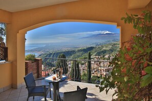 A balcony with a table and chairs, overlooking a scenic view of a mountain and a coastal town. - Villa Angela (Taormina)