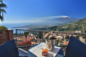 A balcony with a table set for two, overlooking a scenic view of a mountain and the sea. - Villa Angela (Taormina)
