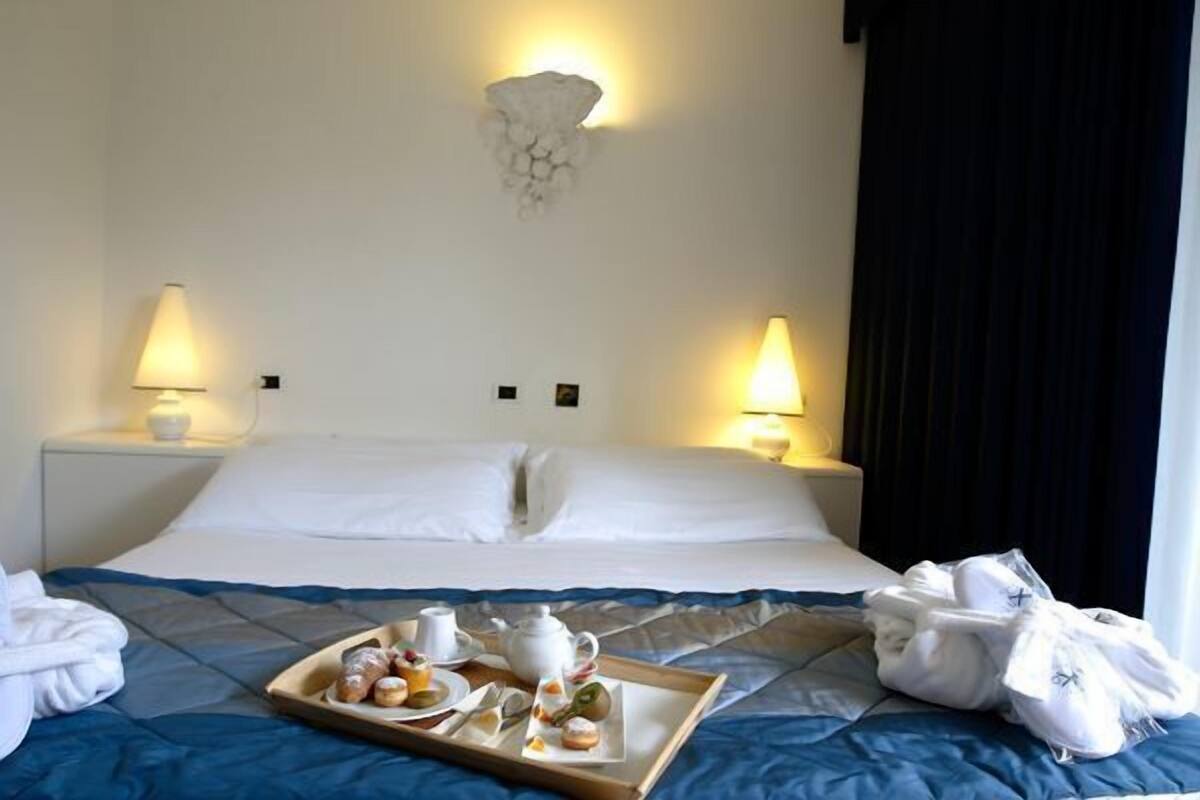 A hotel room with a neatly made bed, two bedside lamps, a tray with breakfast items, and a wall-mounted light fixture.