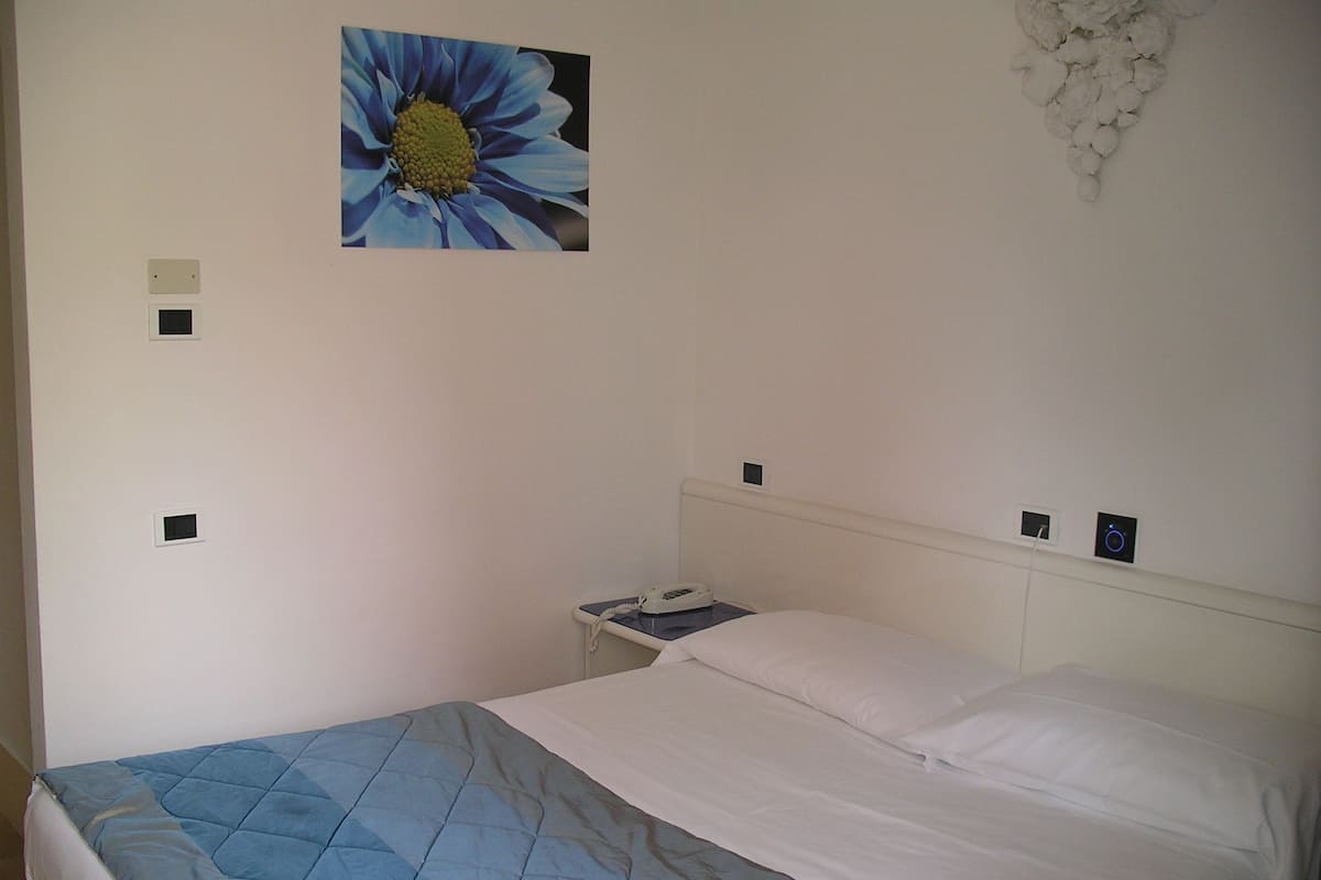 A bedroom with a bed, a nightstand, a wall-mounted phone, and a wall decoration.