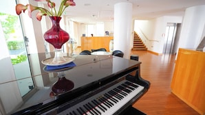 Un piano de cola en un vestíbulo amplio con un mostrador de recepción, una escalera y vistas a zonas verdes.