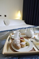 A breakfast tray with pastries, a teapot, and a cup on a bed with a nightstand.