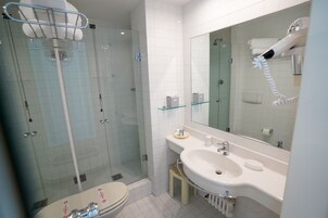 Un bagno moderno con cabina doccia in vetro, lavandino bianco e un ampio specchio.
