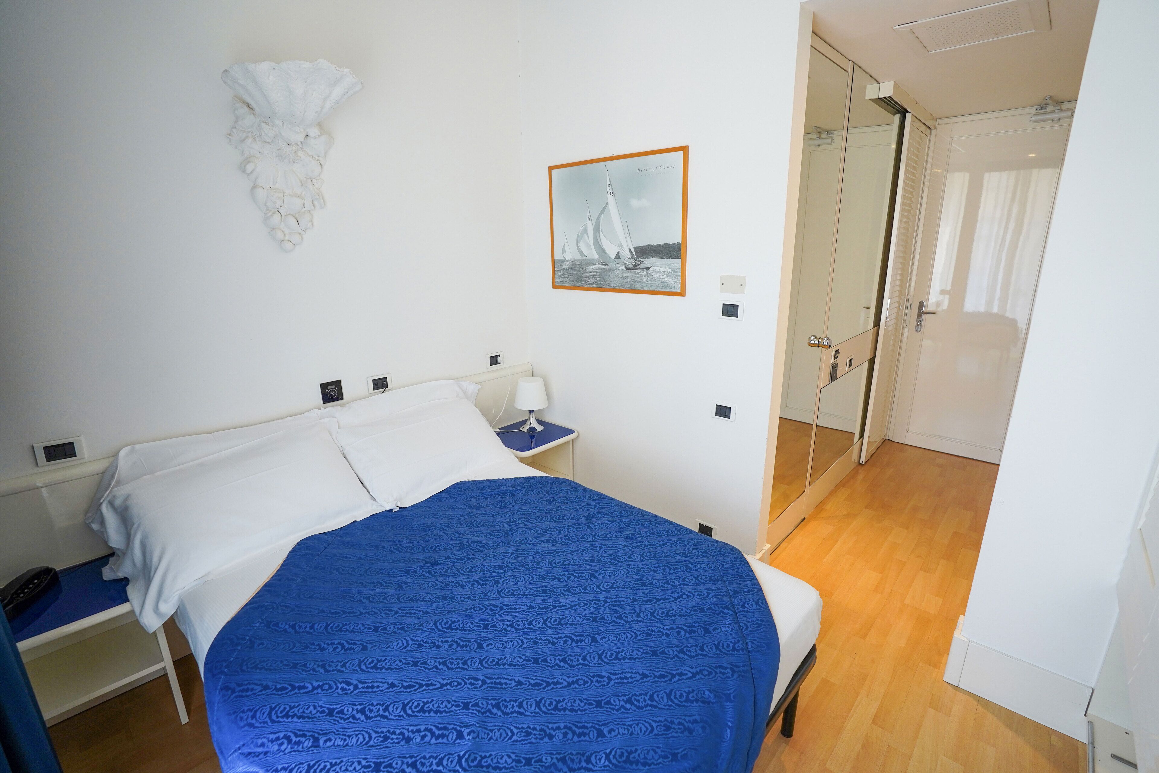 A bedroom with a bed, a nightstand, a wall-mounted artwork, and a door leading to another room.