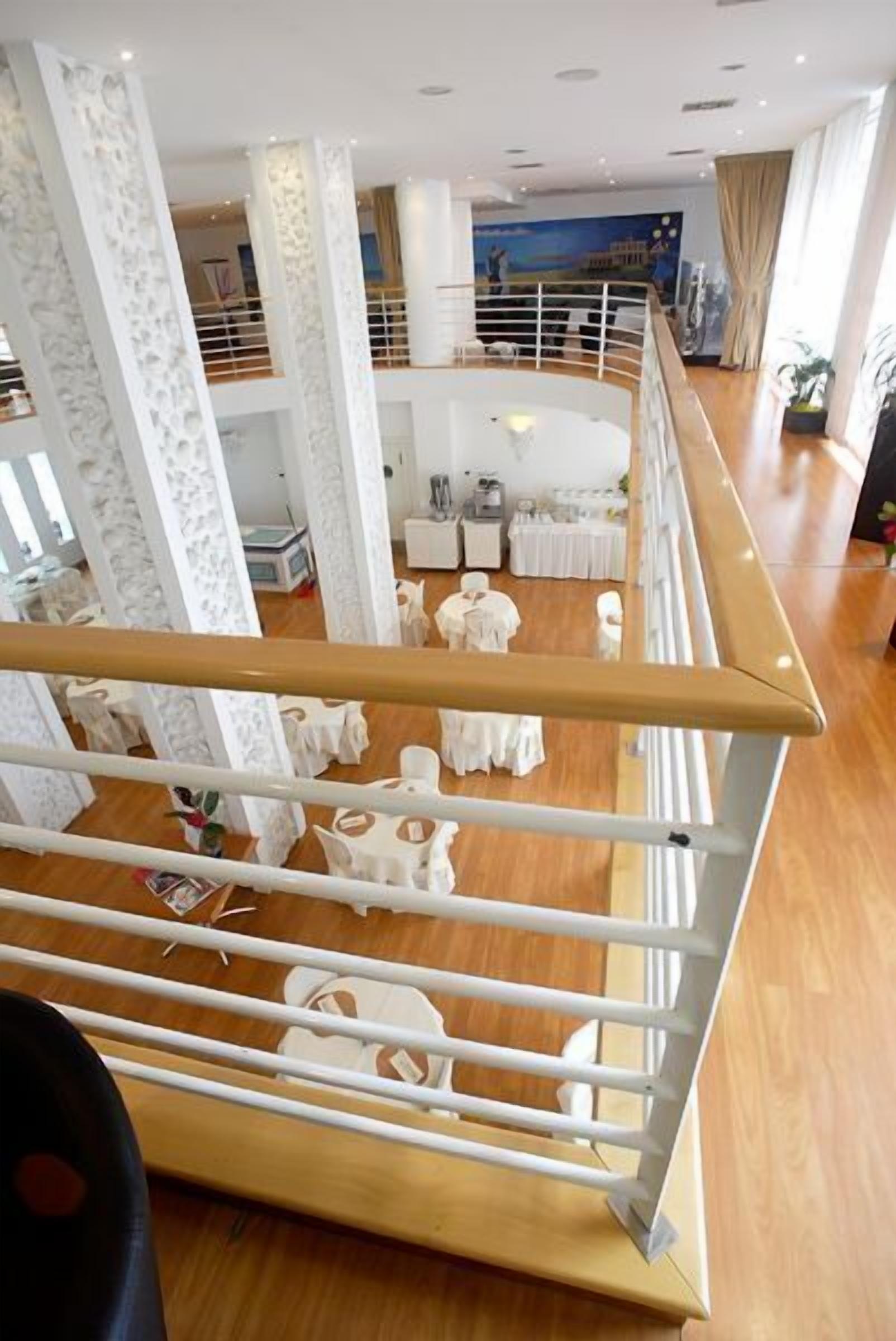 Un hall d’hôtel spacieux, doté d’un plafond haut, de colonnes blanches et d’un espace salon central avec des tables rondes.