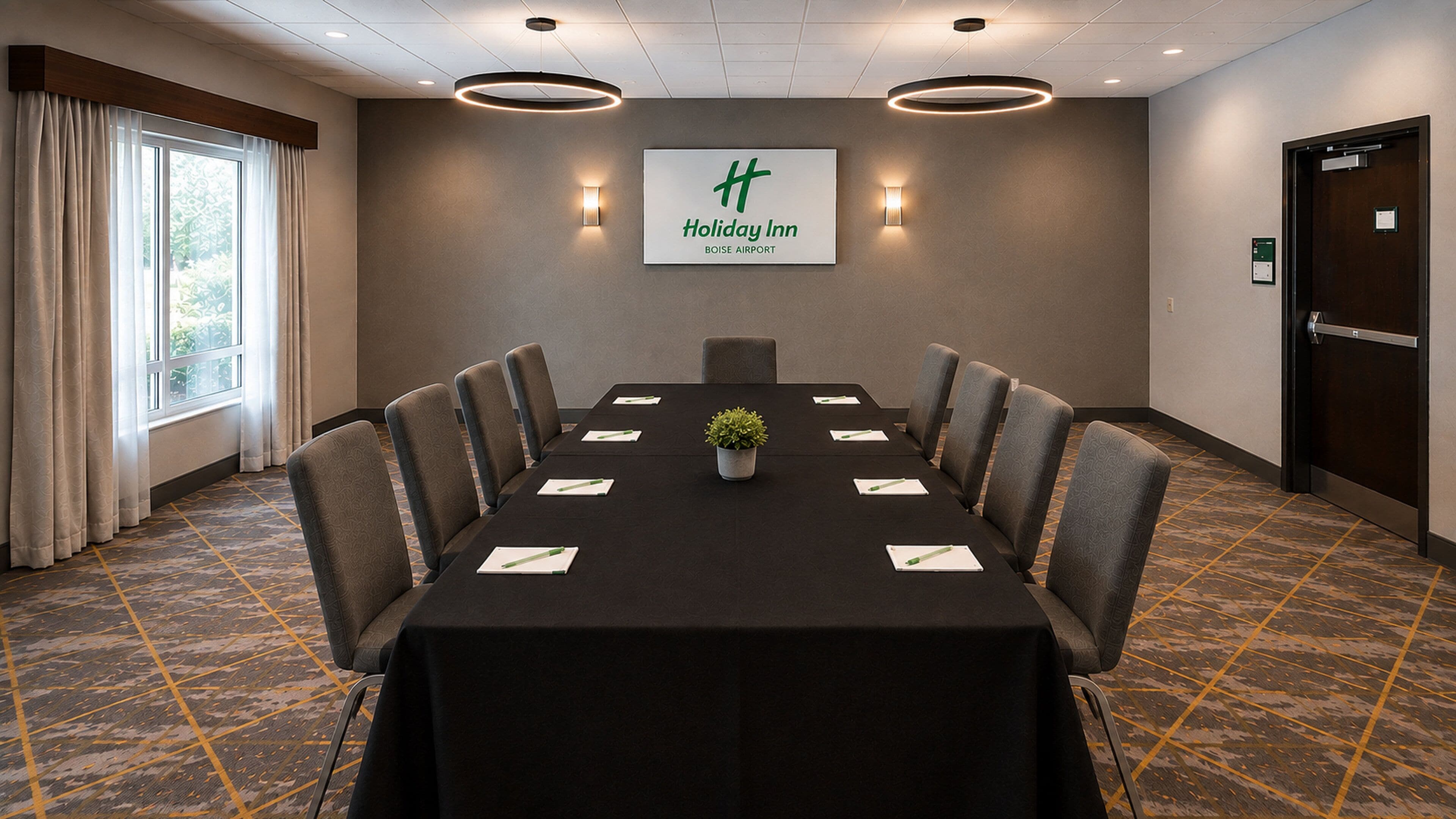 Een vergaderruimte met een lange tafel, stoelen, een potplant en een bord met Holiday Inn Boise Airport.