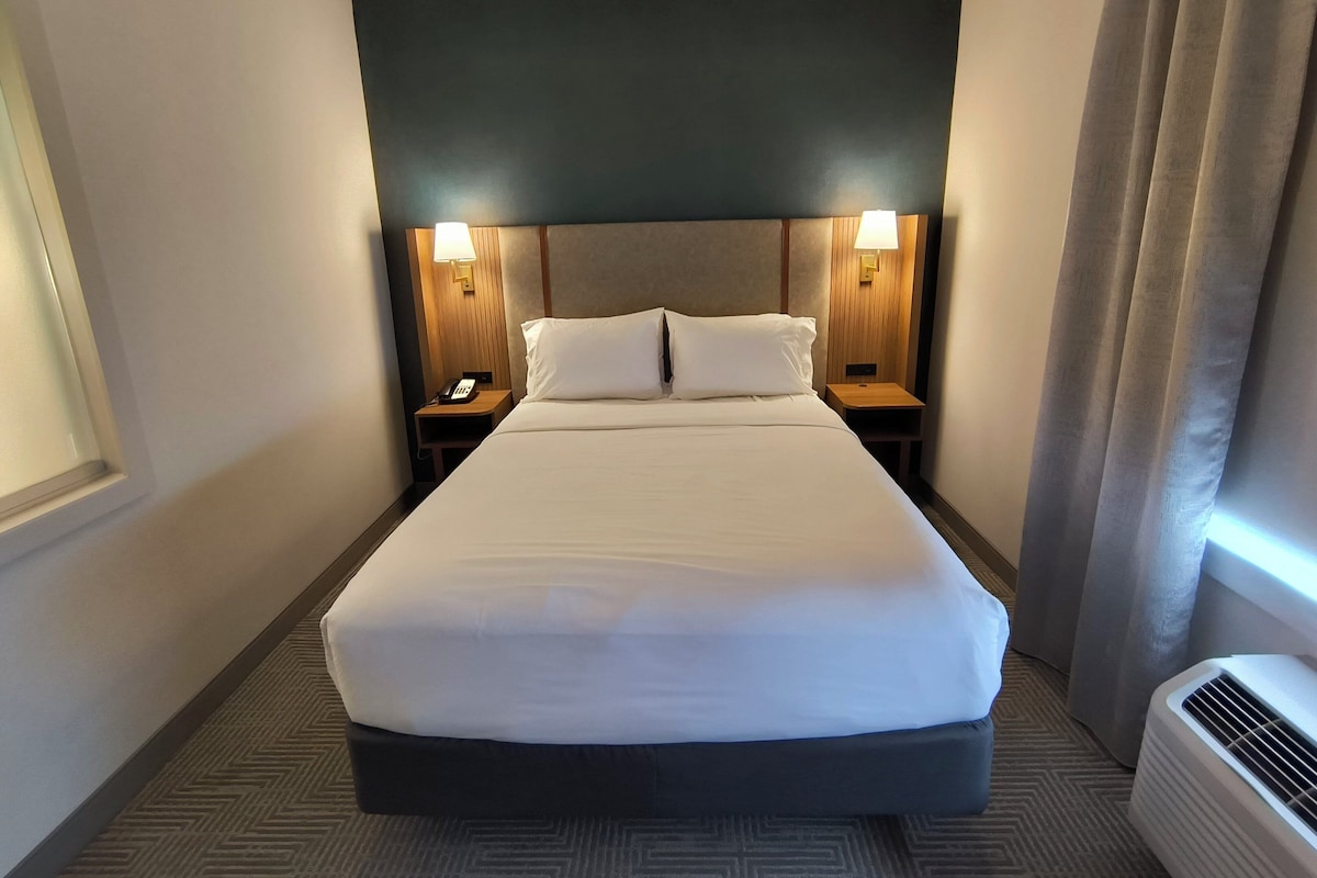 Een hotelkamer met een groot bed, twee nachtkastjes met lampen, een telefoon en een airconditioning.
