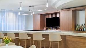 Uma área de bar moderna com balcão de madeira, vários bancos e uma variedade de garrafas de bebidas.
